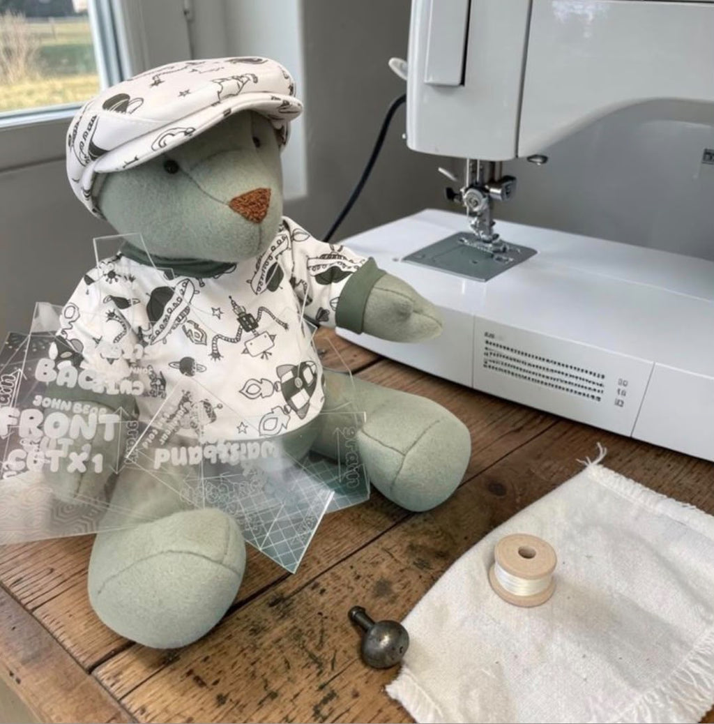 Bear wearing the finished space-print jumper beside acrylic pattern pieces and a sewing machine